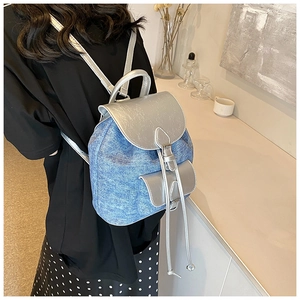 Detail of blue denim backpack with silver metallic straps shown on a model