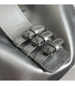 Close-up of silver metallic handbag featuring three rows of polished chrome buckles and stitching