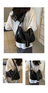 Detail of glossy black hobo bag featuring three rows of metallic buckles on wide strap