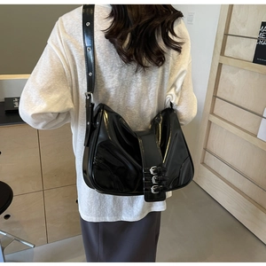 Detail of black patent leather hobo bag featuring three silver metal buckles on the strap