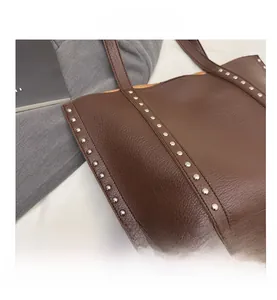Detail view of brown lychee grain leather tote bag featuring stylish silver metal rivets