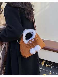 Detail of autumn brown suede dumpling bag with white faux fur trim and cute pom-pom charms