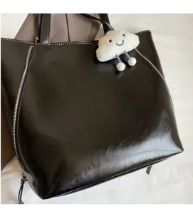 Detail of black tote bag with decorative zippers and a plush white cloud charm accessory