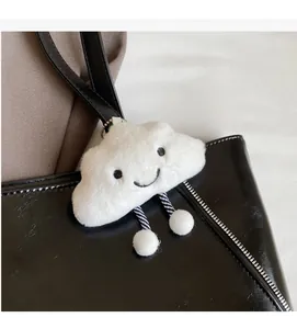 Close-up of white plush cloud charm with smiley face on a black leather tote bag