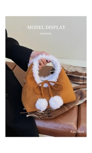 Detail view of brown faux suede handbag with plush white fur trim and fluffy pom-pom charms