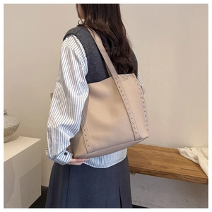 Close-up of beige leather tote bag featuring vertical metal rivets and side seam details
