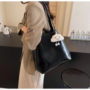 Detail of black glossy tote bag with white cloud plush charm in a minimalist setting