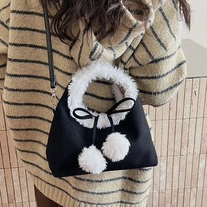 Détail du sac à main noir en suédine avec anses en peluche blanche et pompons doux