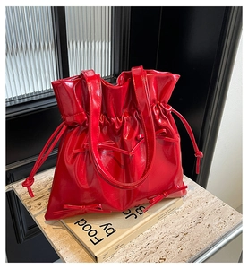 Detail of red glossy bucket bag featuring ballet-style ribbon bows and drawstring design