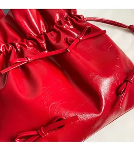 Detail of red glossy patent leather tote bag featuring ballet-style bow accents and pleats