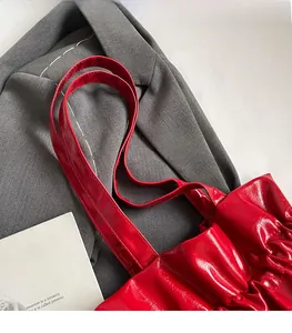 Detail view of red patent leather tote bag featuring pleated texture and slim shoulder straps