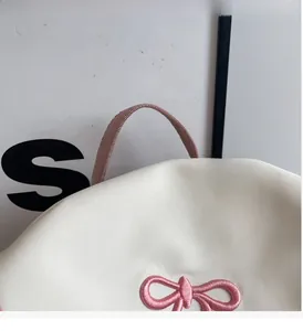 Close-up of white fabric tote bag featuring pink woven handles and bow embroidery details