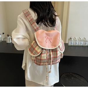 Detail of red and green plaid backpack with a pink flap and 3D bow on a model back