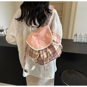 Detail of pink bow accent and plaid canvas backpack worn by model in a cozy cafe