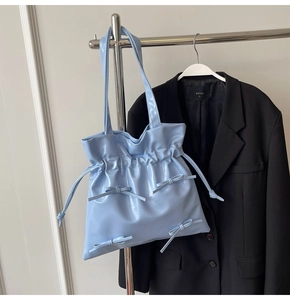 Detail of light blue patent leather tote bag with drawstring closure and bow accents