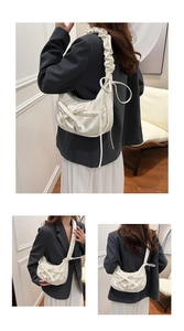 Detail of white pleated shoulder bag featuring a decorative bow and wavy strap texture
