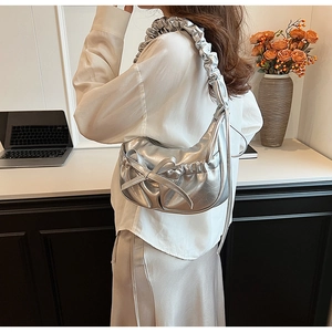 Detail of silver metallic crescent bag featuring pleated handle and large bow detail