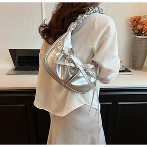 Silver crescent shoulder bag featuring pleated handle and metallic bow detail on a model
