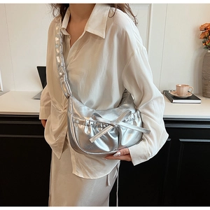 Detail of silver metallic crescent bag featuring pleated texture and a chic bow decoration