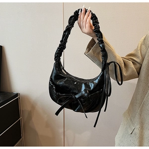 Detail of black glossy hobo bag with pleated handle and bow knot in a half-moon shape