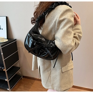 Dettaglio borsa nera lucida con tracolla a pieghe e fiocco decorativo indossata a spalla