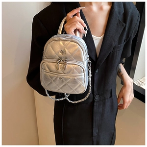 Detail of silver quilted mini bag with flower logo and metallic chain held by model
