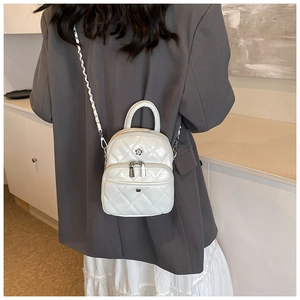 Close-up of white quilted mini bag worn on back showing silver floral logo and chain strap