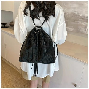 Rear view of a model wearing a glossy black drawstring bucket backpack in a minimalist room