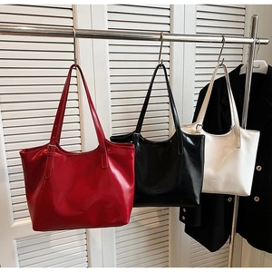 Close-up of three stylish shiny leather tote bags in red, black, and white hanging on a rack
