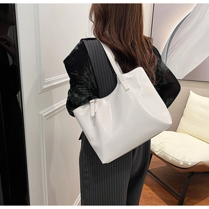 Stylish minimalist large white glossy leather tote bag worn as a trendy underarm shoulder bag