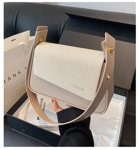 Détail du sac beige avec rabat tissé et rivets dorés dans un coffret cadeau noir