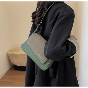 Détail du sac bandoulière en cuir vert et tissage beige avec lettrage doré tendance