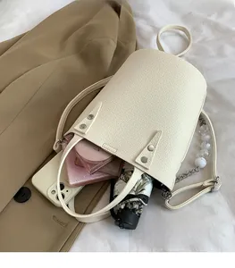 Spacious interior of beige chain bucket bag holding a phone, cosmetics and umbrella