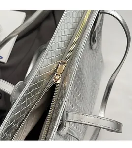 Close-up of silver woven tote bag featuring a smooth gold-tone metal zipper and texture