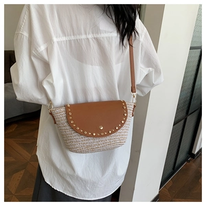 Detail of woven crossbody bag with brown leather flap and decorative gold rivets