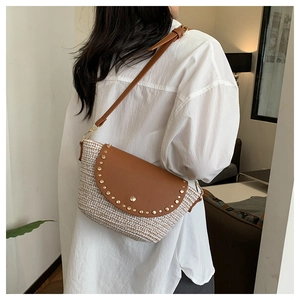 Detail of woven straw crossbody bag with brown leather flap and golden rivet accents