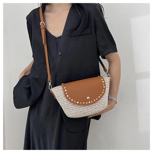 Detail of woven straw bag with brown leather flap and gold metal rivets on black blazer