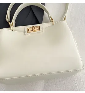Detailed view of cream leather shoulder bag featuring a gold turn-lock closure on fabric