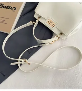 Detail of white leather handbag featuring gold metal turn-lock and adjustable strap