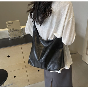 Detail view of large black pleated tote bag with embossed shiny texture on model
