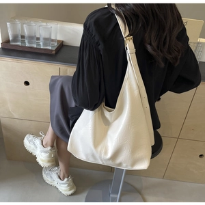 Detail of adjustable gold buckle and wrinkled leather texture on a white hobo bag