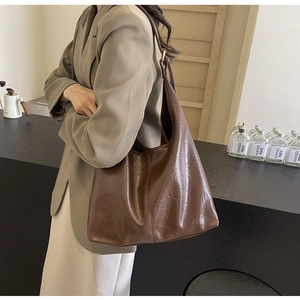 Détail d'un grand sac hobo marron foncé avec texture cuir plissé porté à l'épaule