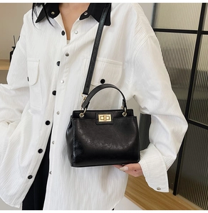 Detail of elegant black leather handbag with golden twist-lock closure on white blouse