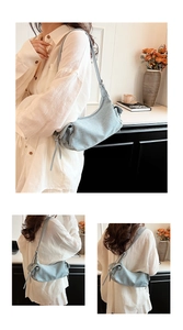 Detail of light blue textured shoulder bag with drawstring side and sleek half-moon shape