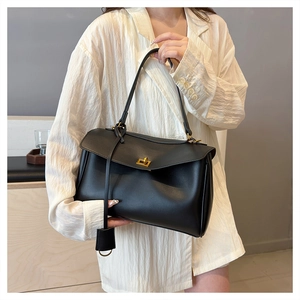 Close-up of black leather handbag featuring a golden rectangular twist lock and flap closure