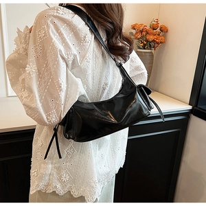 Detail of minimalist black PU leather shoulder bag with glossy finish on a female model