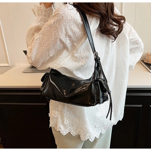 Close-up of a black glossy faux leather shoulder bag with side flap pocket details