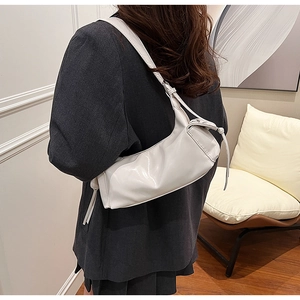 Detail der weißen glänzenden Schultertasche mit Plissee-Design zu einem grauen Blazer