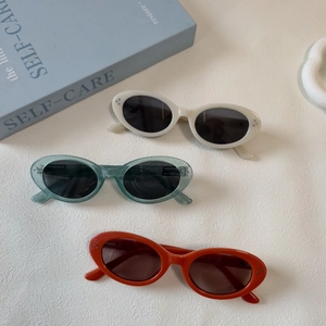 Flat lay of retro oval sunglasses in cream, green, and orange with silver rivet details
