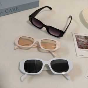 Three pairs of bold rectangular sunglasses in black, beige, and white on a lifestyle background